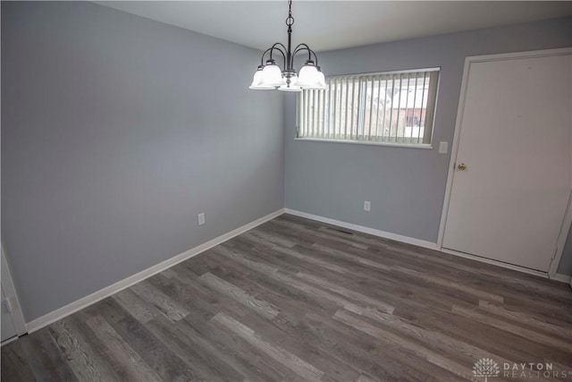 spare room with a chandelier, dark wood-type flooring, and baseboards