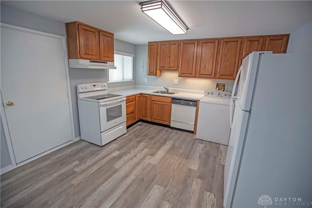 kitchen with under cabinet range hood, white appliances, light countertops, brown cabinetry, and washer / dryer