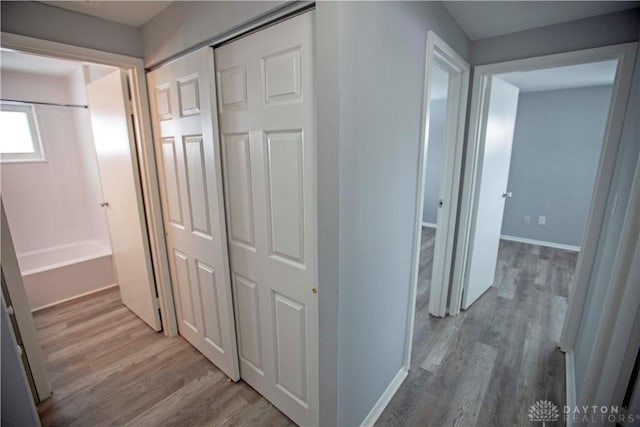 corridor featuring light wood-type flooring and baseboards