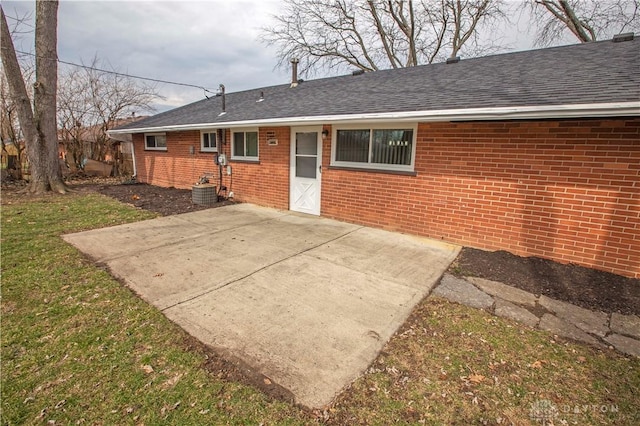 back of house with a yard, a shingled roof, a patio, and brick siding