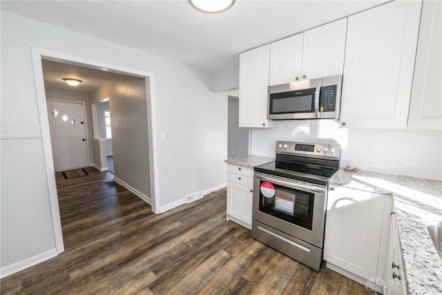 kitchen featuring dark wood-type flooring, appliances with stainless steel finishes, white cabinets, and light stone counters