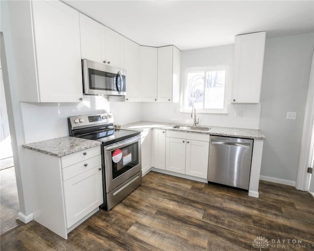 kitchen featuring light stone counters, dark wood finished floors, stainless steel appliances, white cabinets, and a sink