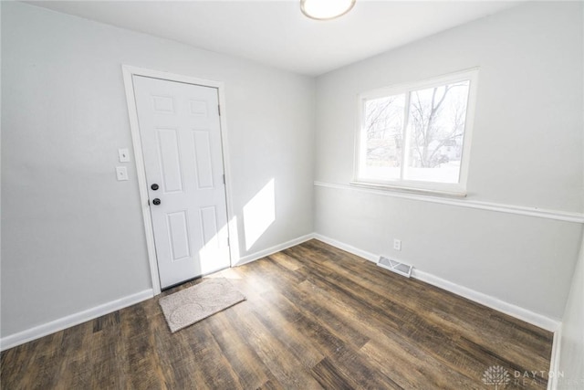 spare room featuring dark wood-style flooring, visible vents, and baseboards