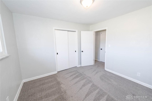 unfurnished bedroom with baseboards, a closet, and light colored carpet