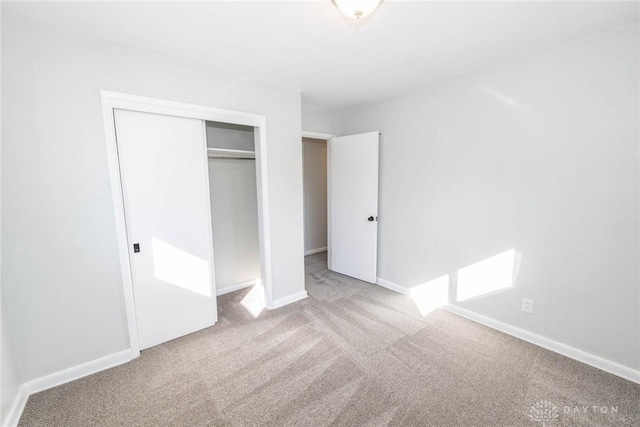 unfurnished bedroom featuring baseboards, a closet, and light colored carpet