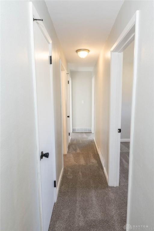 hall featuring dark colored carpet and baseboards