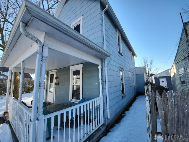 view of snowy exterior featuring covered porch and fence