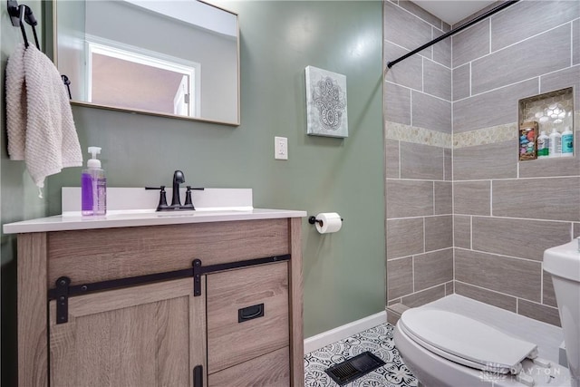 bathroom featuring baseboards, toilet, tile patterned floors, a tile shower, and vanity