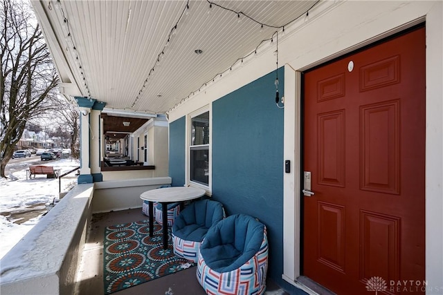 snow covered property entrance featuring a porch and stucco siding