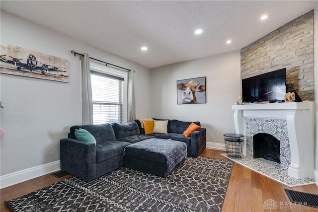 living room featuring a textured ceiling, a fireplace, visible vents, baseboards, and dark wood finished floors