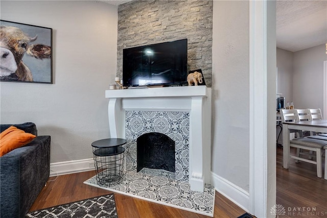 living area with wood finished floors, a tile fireplace, and baseboards