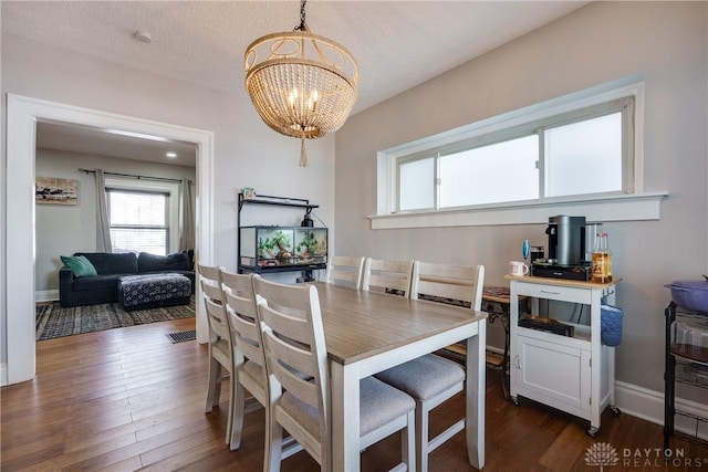 dining space featuring a notable chandelier, a textured ceiling, baseboards, and dark wood-style flooring