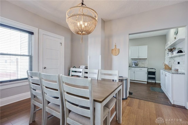 dining space featuring a textured ceiling, baseboards, dark wood finished floors, and a notable chandelier