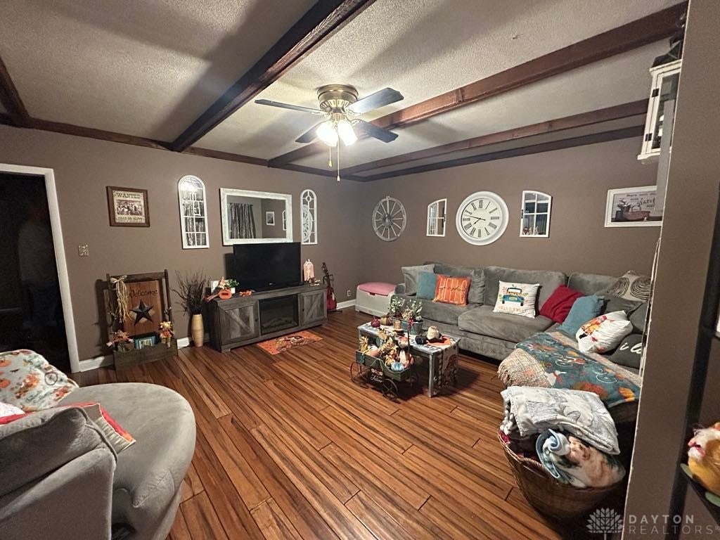 living area featuring a textured ceiling, wood finished floors, a ceiling fan, baseboards, and beamed ceiling