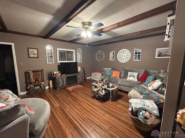 living area featuring a textured ceiling, wood finished floors, a ceiling fan, baseboards, and beamed ceiling