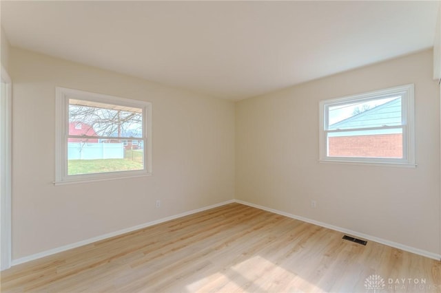 empty room featuring light wood finished floors, baseboards, and a wealth of natural light