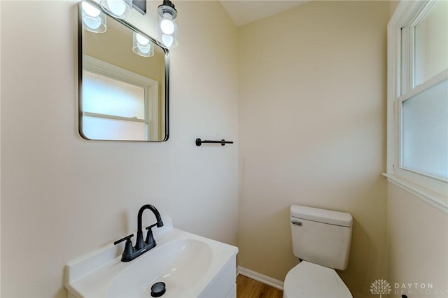 half bathroom with wood finished floors, a sink, toilet, and baseboards