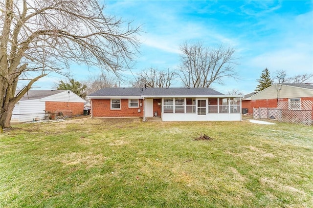 back of property featuring a sunroom, fence, a lawn, and brick siding