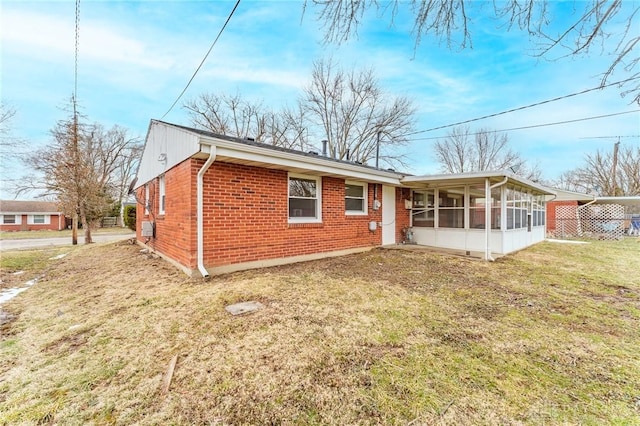 back of house featuring a yard, brick siding, and a sunroom