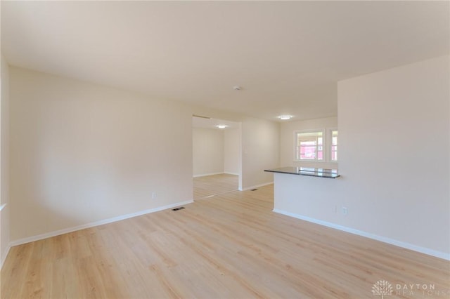 spare room featuring light wood-type flooring, visible vents, and baseboards