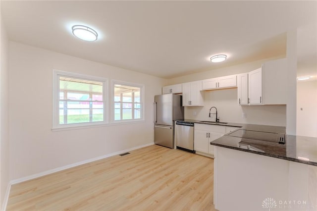 kitchen featuring appliances with stainless steel finishes, white cabinets, a sink, and dark stone countertops