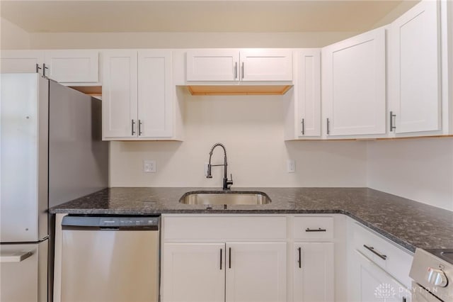 kitchen featuring dark stone counters, white cabinets, a sink, and stainless steel dishwasher