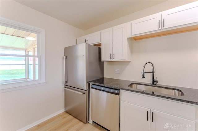 kitchen with stainless steel appliances, dark stone countertops, a sink, and white cabinets