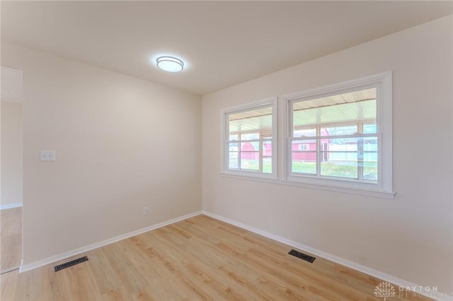 empty room featuring light wood finished floors, visible vents, and baseboards