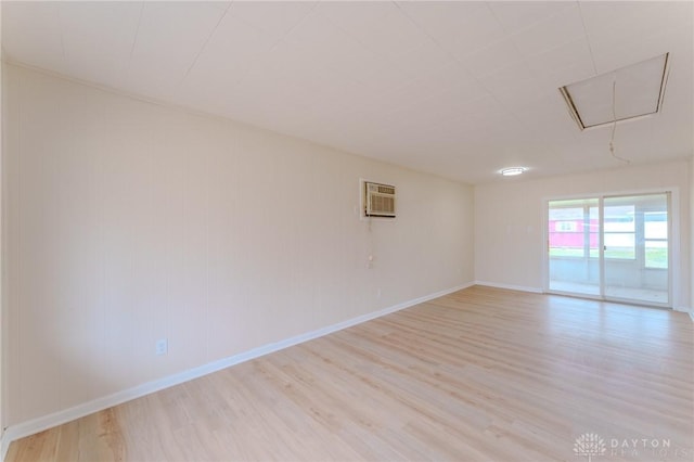 unfurnished room with attic access, baseboards, light wood finished floors, and a wall mounted AC