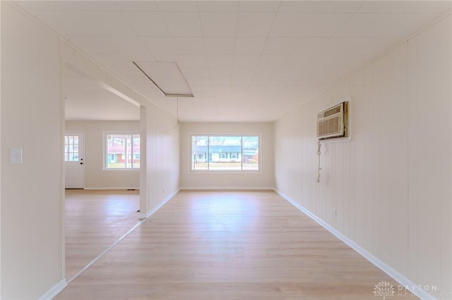 empty room featuring a wall unit AC, light wood finished floors, attic access, and baseboards