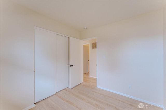 unfurnished bedroom featuring a closet, visible vents, light wood-style flooring, and baseboards