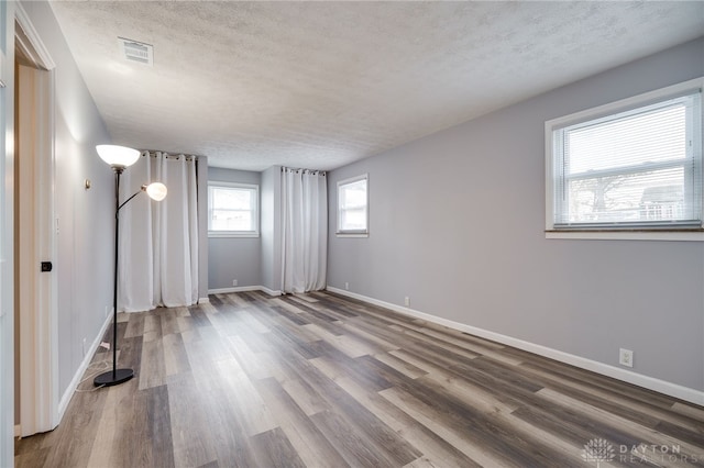 spare room with baseboards, a textured ceiling, visible vents, and wood finished floors