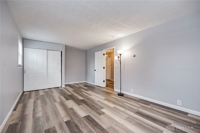 unfurnished bedroom featuring light wood finished floors, a closet, and baseboards