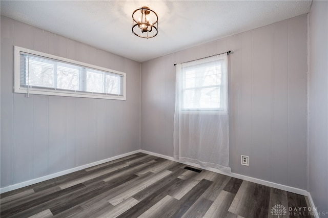 spare room featuring dark wood-type flooring, visible vents, plenty of natural light, and baseboards