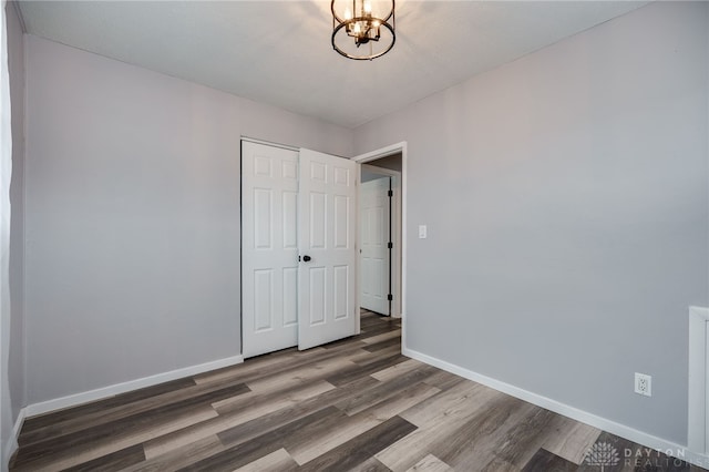 unfurnished bedroom with a notable chandelier, a closet, dark wood finished floors, and baseboards