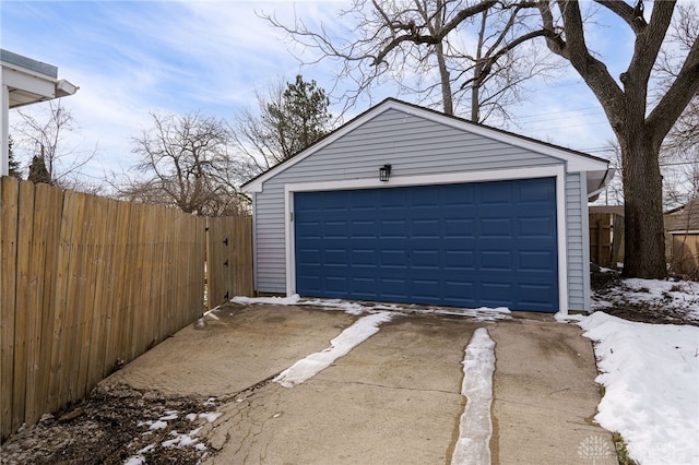 snow covered garage featuring a garage and fence