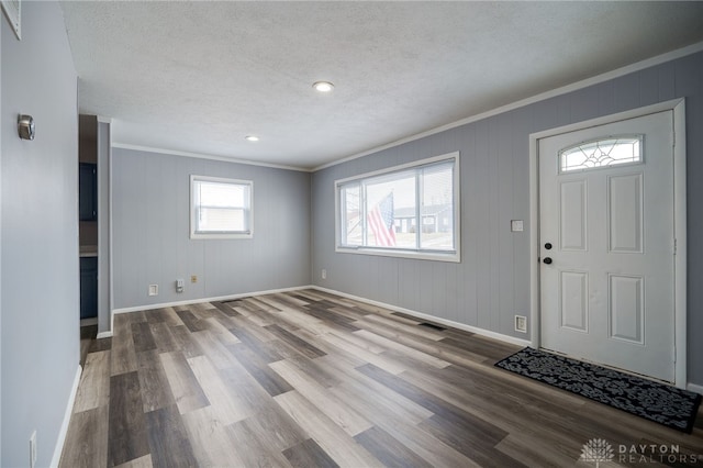 entryway featuring a textured ceiling, wood finished floors, visible vents, baseboards, and ornamental molding