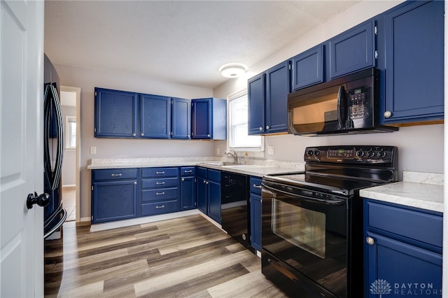 kitchen with a sink, baseboards, light wood-style floors, blue cabinetry, and black appliances