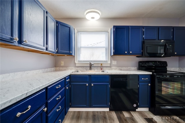 kitchen with dark wood finished floors, blue cabinetry, light countertops, a sink, and black appliances