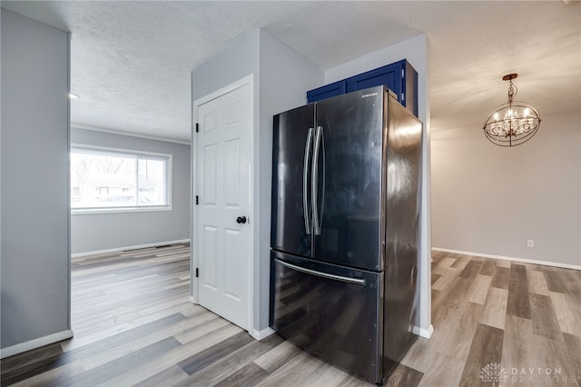 kitchen with baseboards, light wood-style flooring, freestanding refrigerator, a textured ceiling, and blue cabinetry