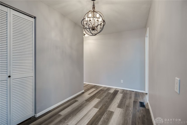 unfurnished dining area with a chandelier, visible vents, baseboards, and wood finished floors