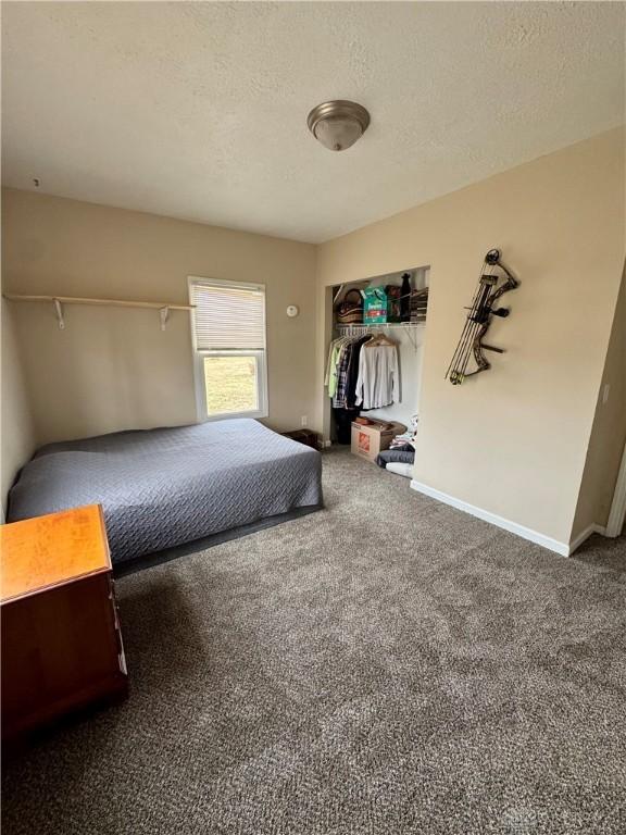 unfurnished bedroom with dark carpet, a textured ceiling, and baseboards