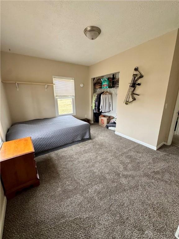 unfurnished bedroom with a closet, dark carpet, a textured ceiling, and baseboards