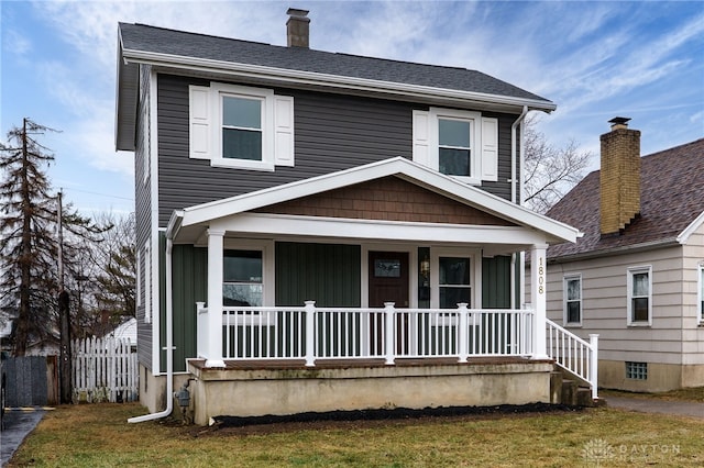 view of front of house with covered porch, a chimney, a front lawn, and roof with shingles