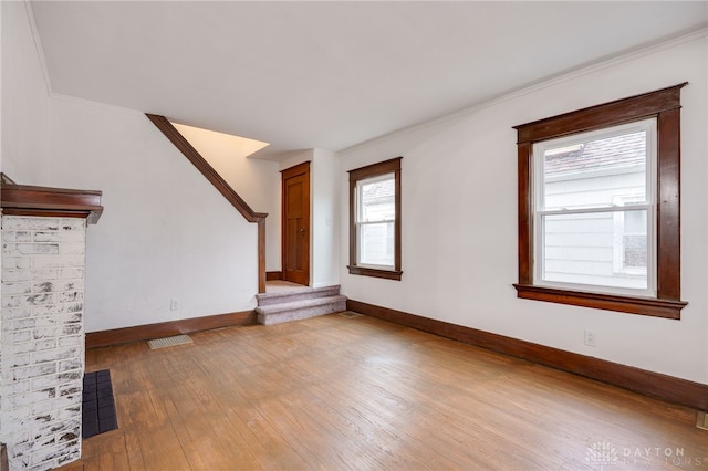 unfurnished living room with crown molding, visible vents, wood finished floors, baseboards, and stairs