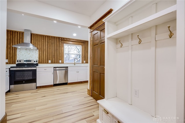 kitchen with stainless steel appliances, white cabinetry, light countertops, wall chimney exhaust hood, and light wood finished floors