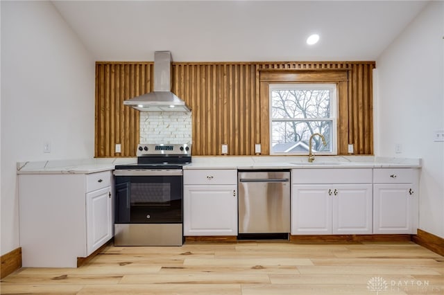 kitchen with white cabinets, stainless steel appliances, light countertops, wall chimney range hood, and a sink