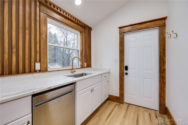 kitchen featuring light stone counters, lofted ceiling, white cabinets, a sink, and dishwasher