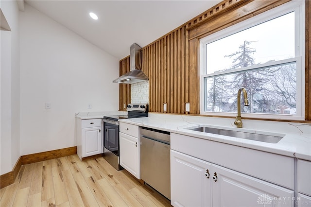 kitchen with appliances with stainless steel finishes, white cabinetry, vaulted ceiling, a sink, and wall chimney range hood