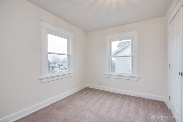 spare room featuring a healthy amount of sunlight, baseboards, and light colored carpet